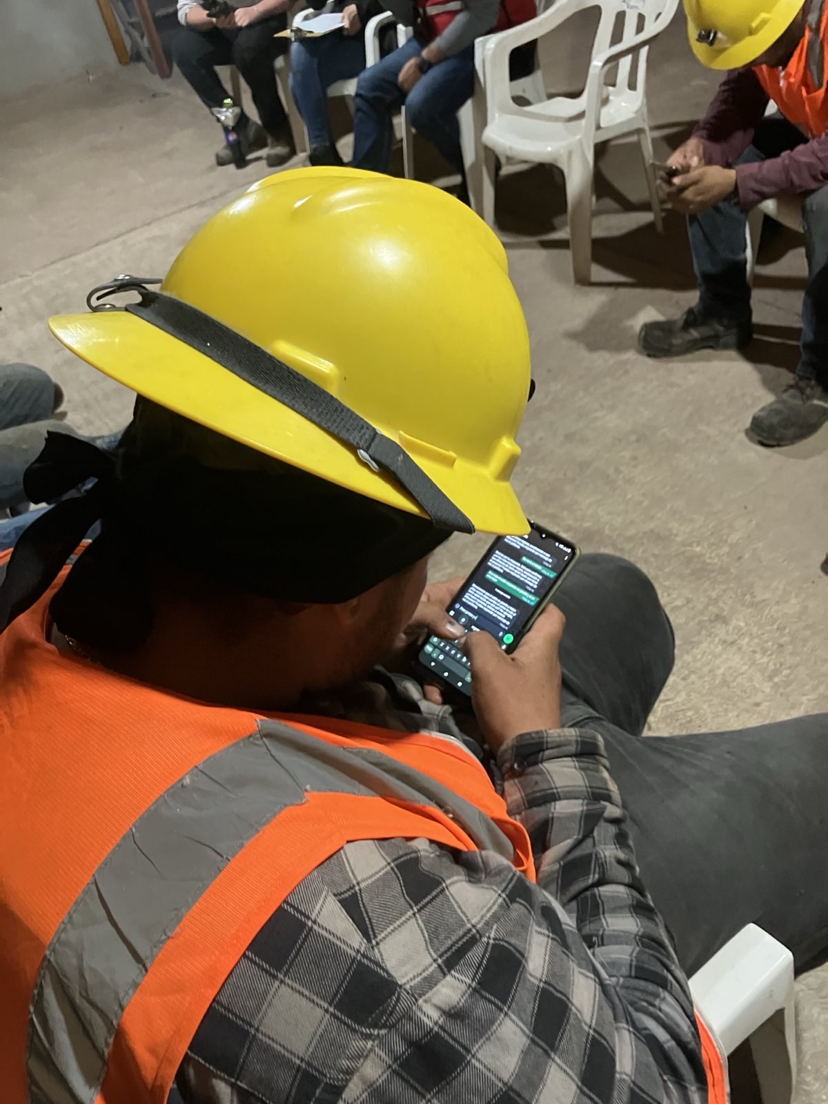 A forestry worker in a yellow hardhat and orange high-vis vest using WhatsApp on his phone during a Fieldloop interview session in Durango